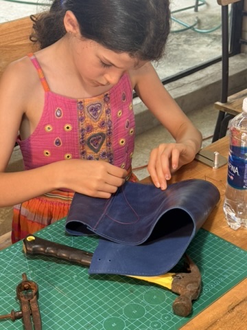 A child hand-stitching blue leather at a workbench