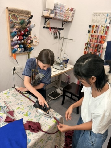 A child pressing fabric beside a sewing teacher in a Hoi An studio